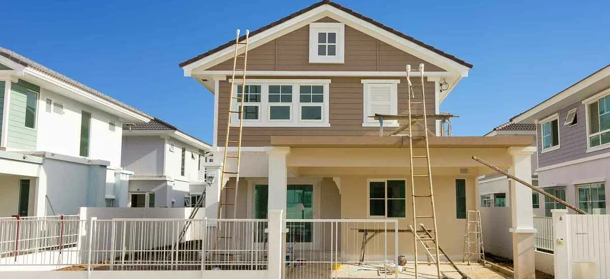 House exterior being painted, with ladders set up against the siding